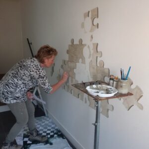 ik ben aan het werk in een bedrijf om de puzzelstukjes op de gangmuur te schilderen, later komen hier logo's, cartoonfiguurtjes en takken bij